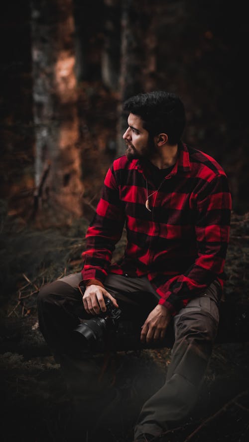 Man in Plaid Long Sleeve Shirt Sitting and Holding a Camera