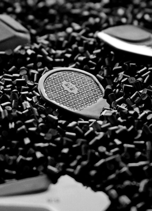 Free Black and white image highlighting a guitar pick amidst scattered black pellets, showcasing intricate design. Stock Photo