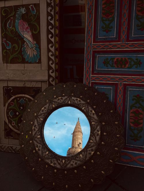 Free Circular mirror reflecting a minaret, surrounded by intricate painted panels, creating an artistic composition. Stock Photo