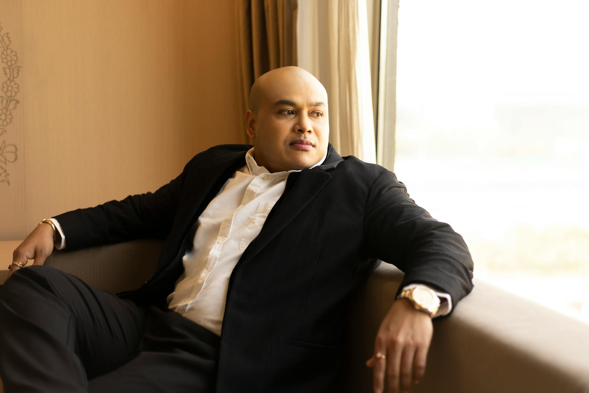 Confident businessman sitting indoors, gazing outside with a thoughtful expression.