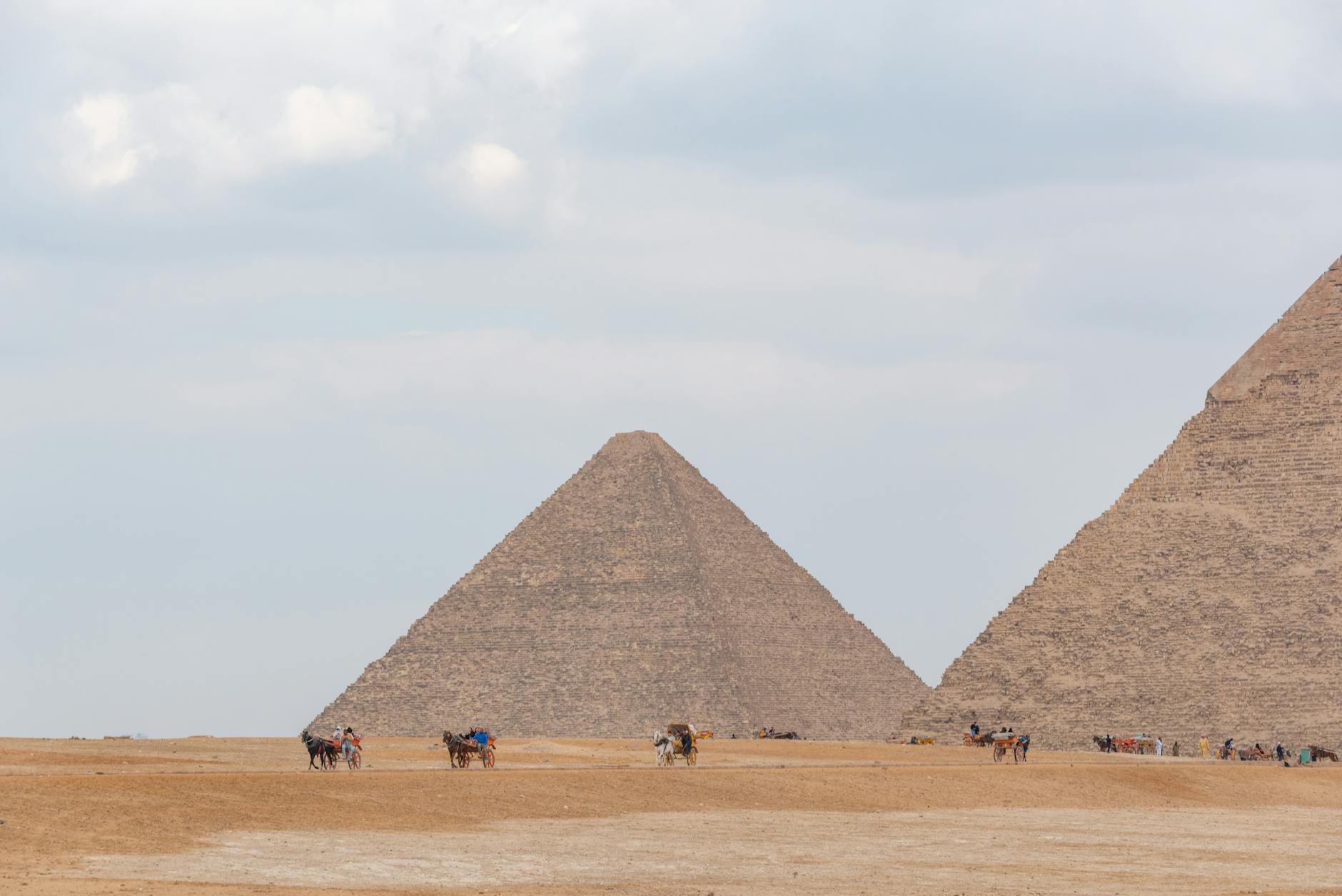 Camel riders near the iconic pyramids of Giza under a cloudy sky, showcasing Egypt's historical allure.
