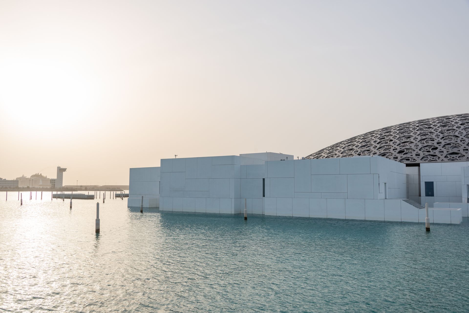 Futuristic white building with dome reflected in water at sunset, serene ambiance.