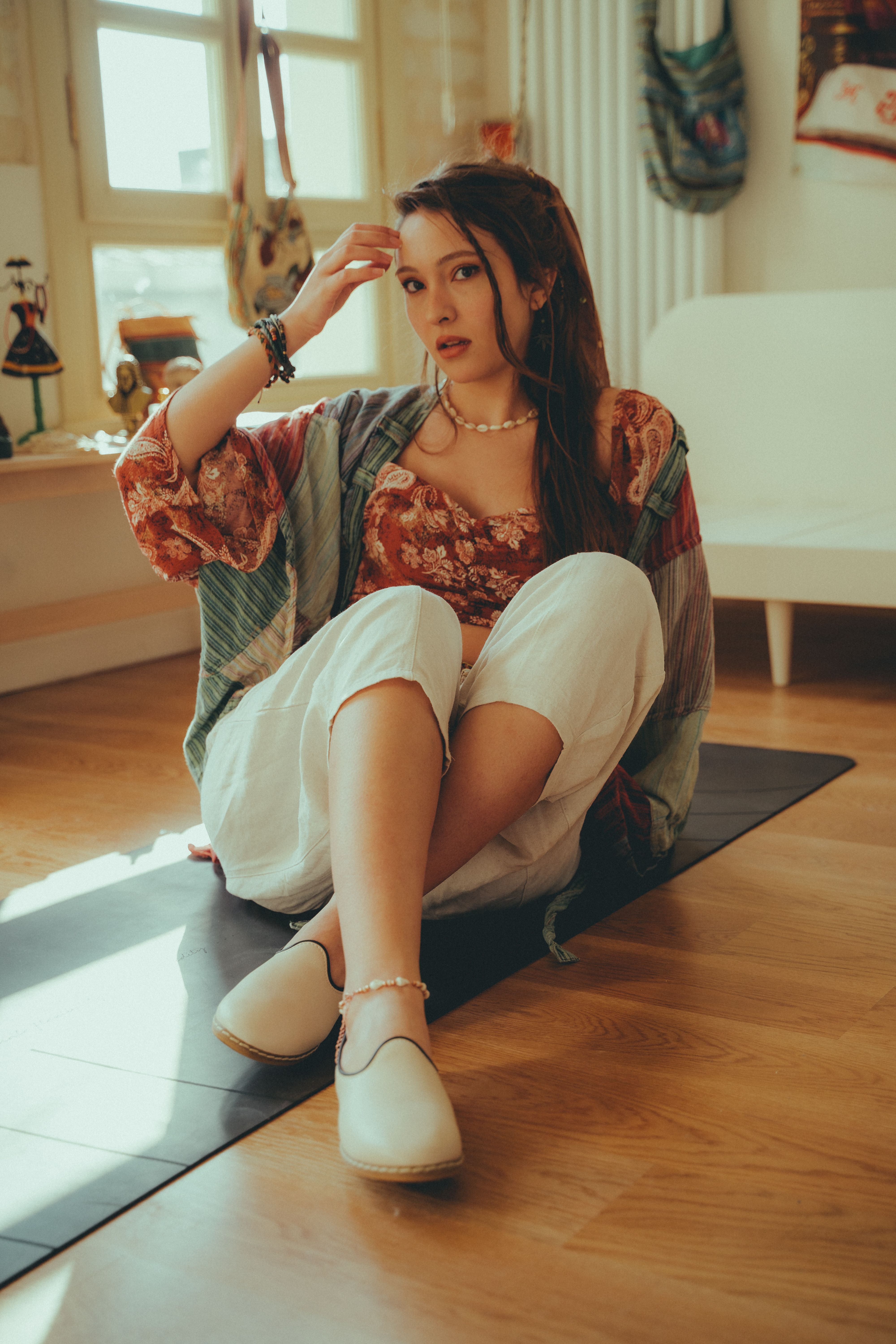 Relaxed young woman sitting on a mat indoors, wearing casual attire with a warm and ambient atmosphere.