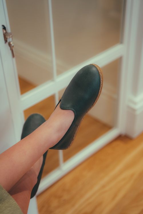 Free Close-up of a person's legs in black slip-on shoes by a white-framed window indoors. Stock Photo