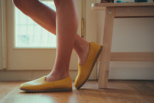 Free Elegant legs wearing bright yellow shoes indoors, showcasing modern footwear style. Stock Photo