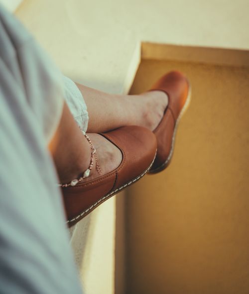 Free Close-up view of a woman's legs wearing brown loafers and anklet, relaxed on a ledge. Stock Photo