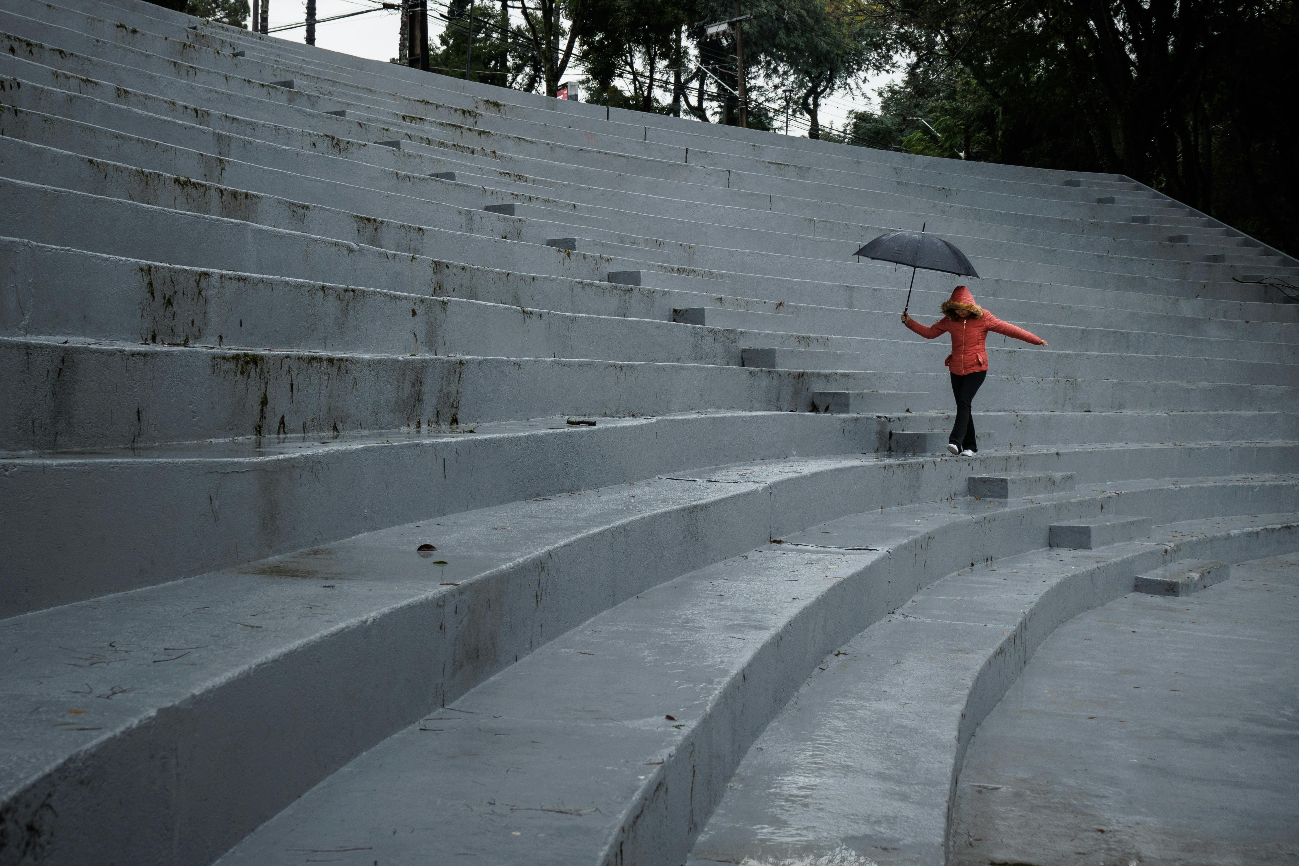 Free A woman with an umbrella walks up gray steps on a rainy day in Curitiba, Brazil. Stock Photo