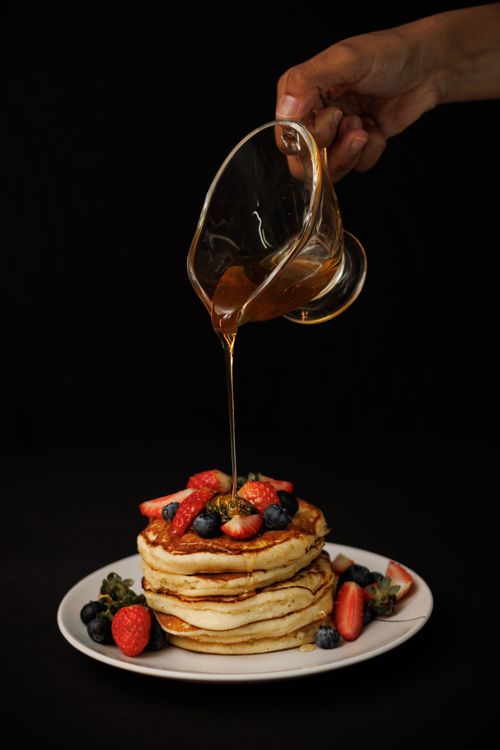 Free Stack of fluffy pancakes topped with fresh berries and syrup pouring on black background. Stock Photo