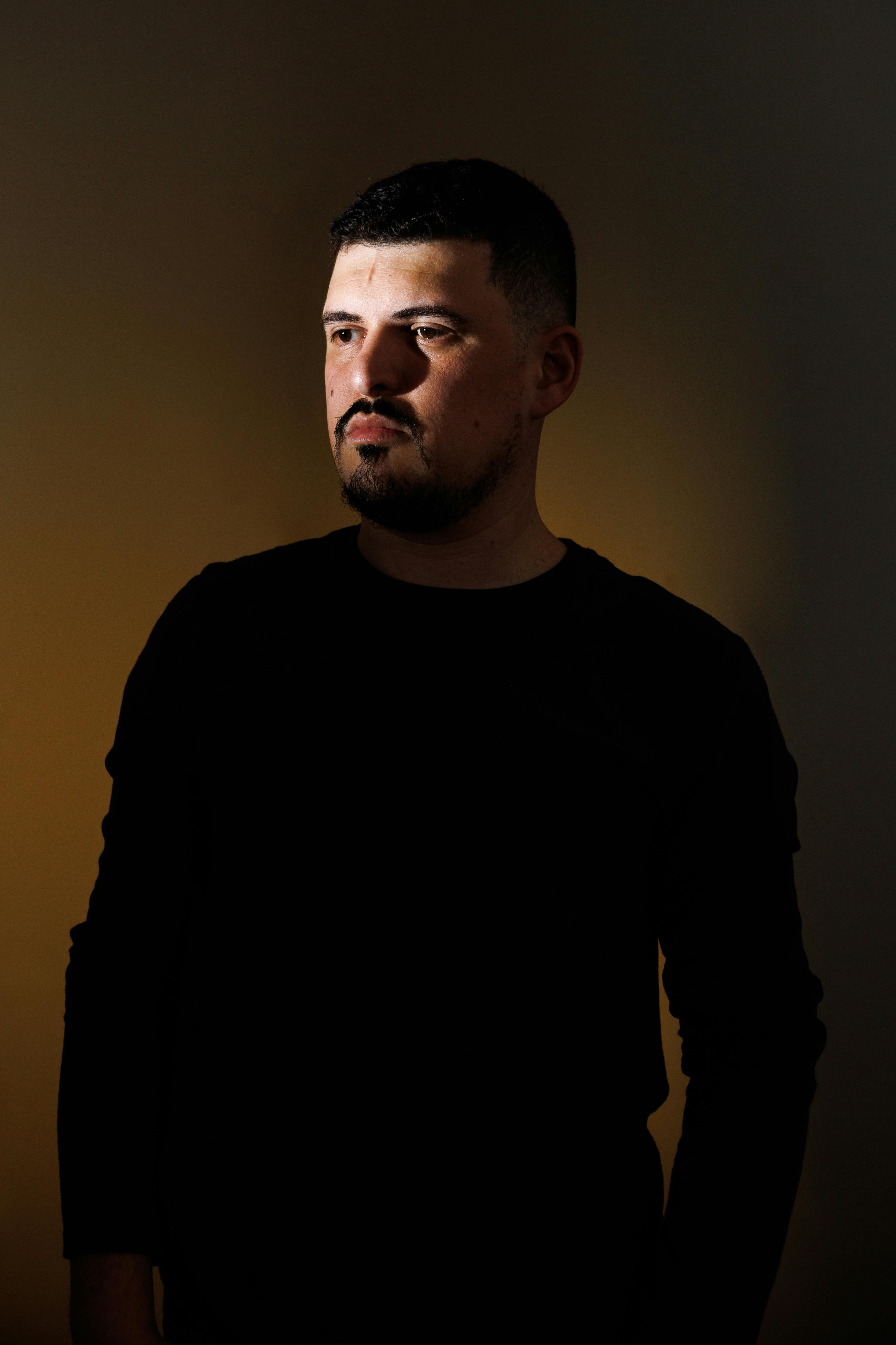 Dramatic portrait of a man with a mustache under focused lighting, creating deep shadows.