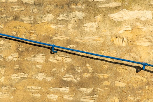 Close-up of a stone wall with a blue handrail, sunlit and textured.