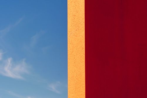 Free Minimalist composition of a vivid red and orange wall against a bright blue sky. Stock Photo