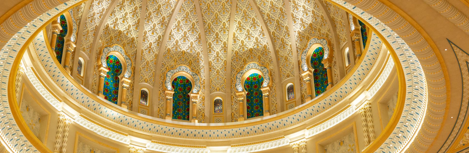 Stunning interior view of a golden mosque dome showcasing intricate patterns and stained glass windo