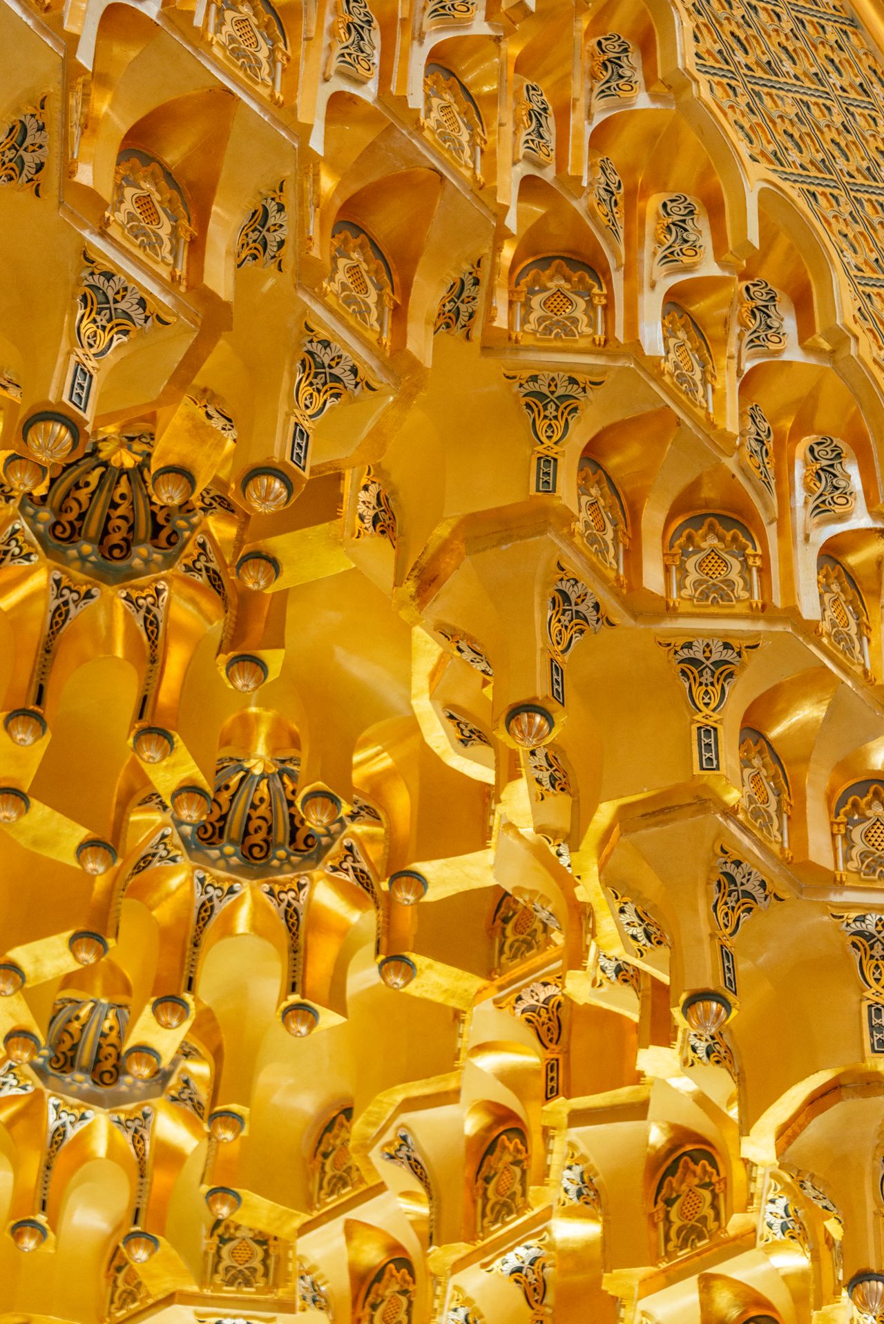 A detailed view of an ornate gold ceiling with intricate Islamic patterns inside a mosque.