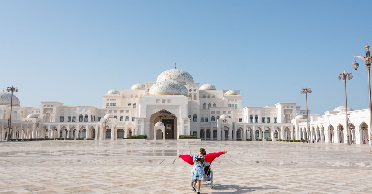 A child runs joyfully in the grand courtyard of a Middle Eastern palace under a clear blue sky.