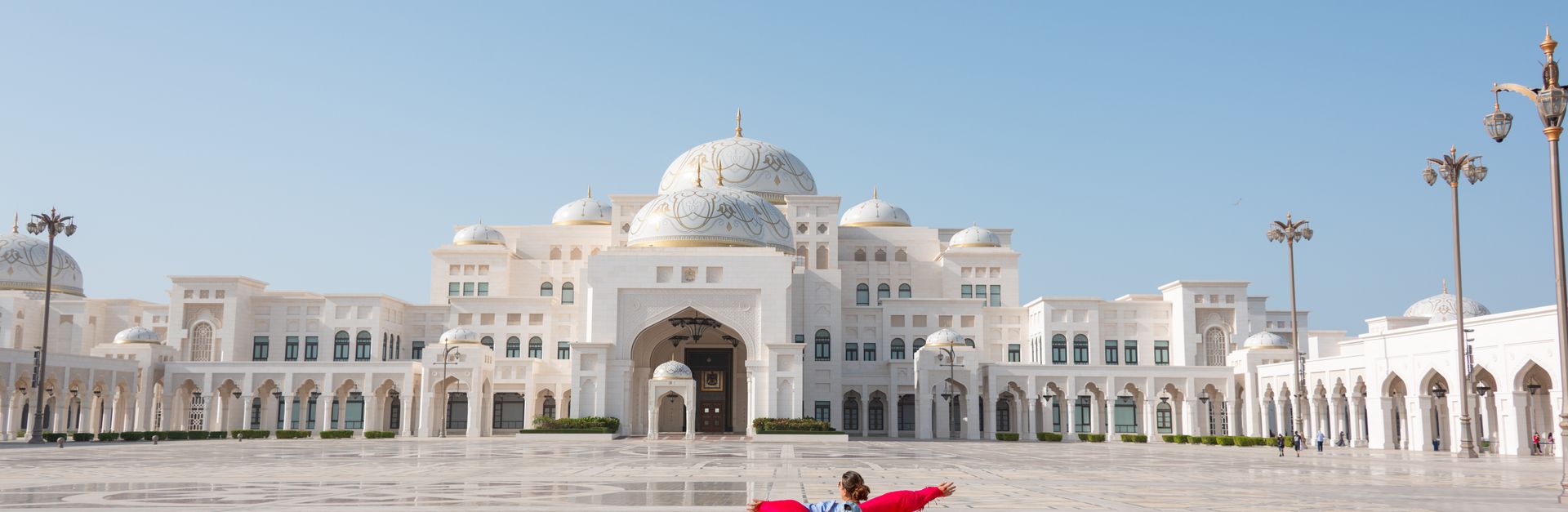 A child runs joyfully in the grand courtyard of a Middle Eastern palace under a clear blue sky.