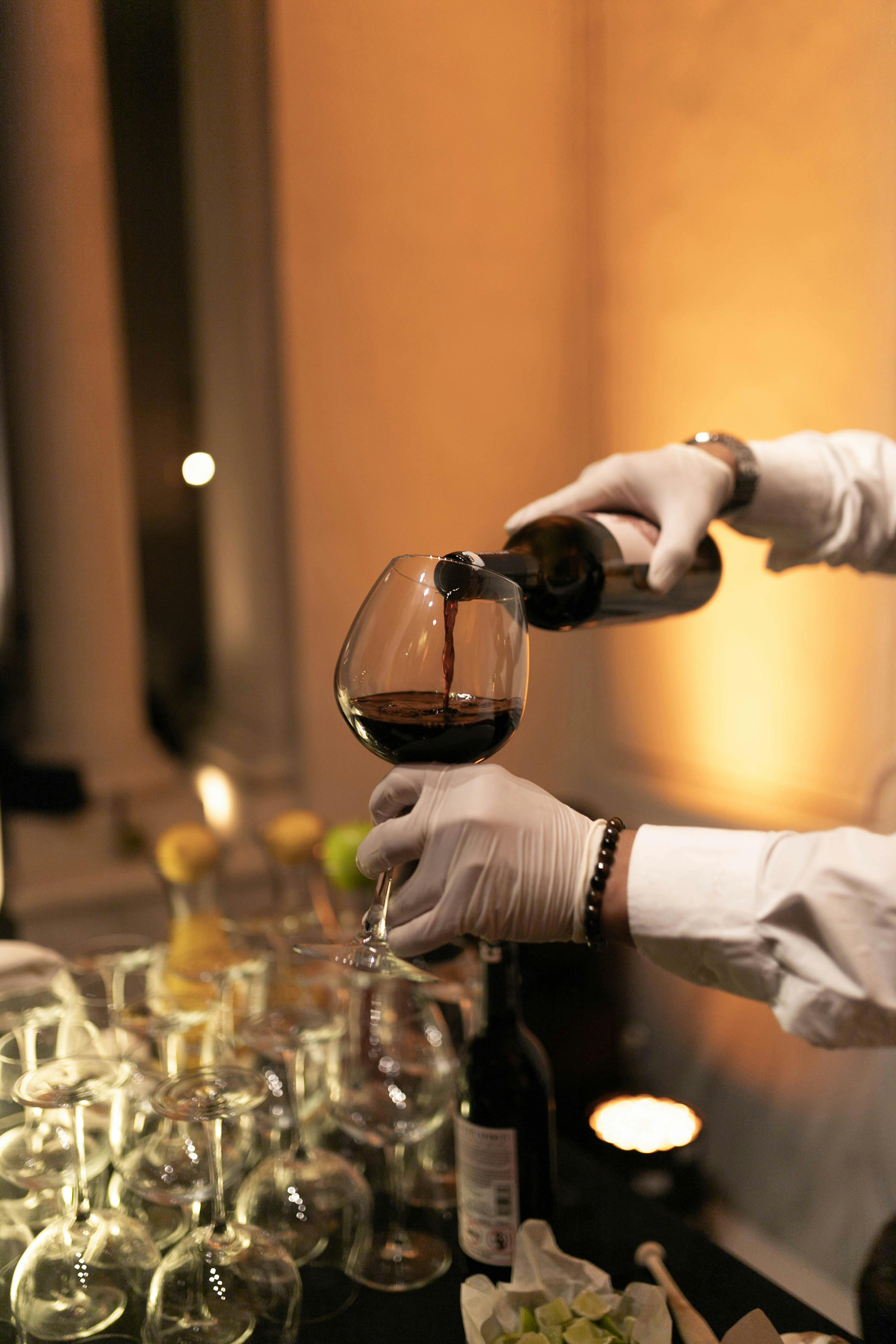 a person in white gloves pouring wine into glasses