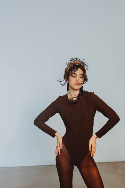 Fashion photography of a woman posing in a brown bodysuit in a minimalist studio.
