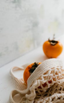 Close-up shot of ripe persimmons in a net bag against a soft backdrop.