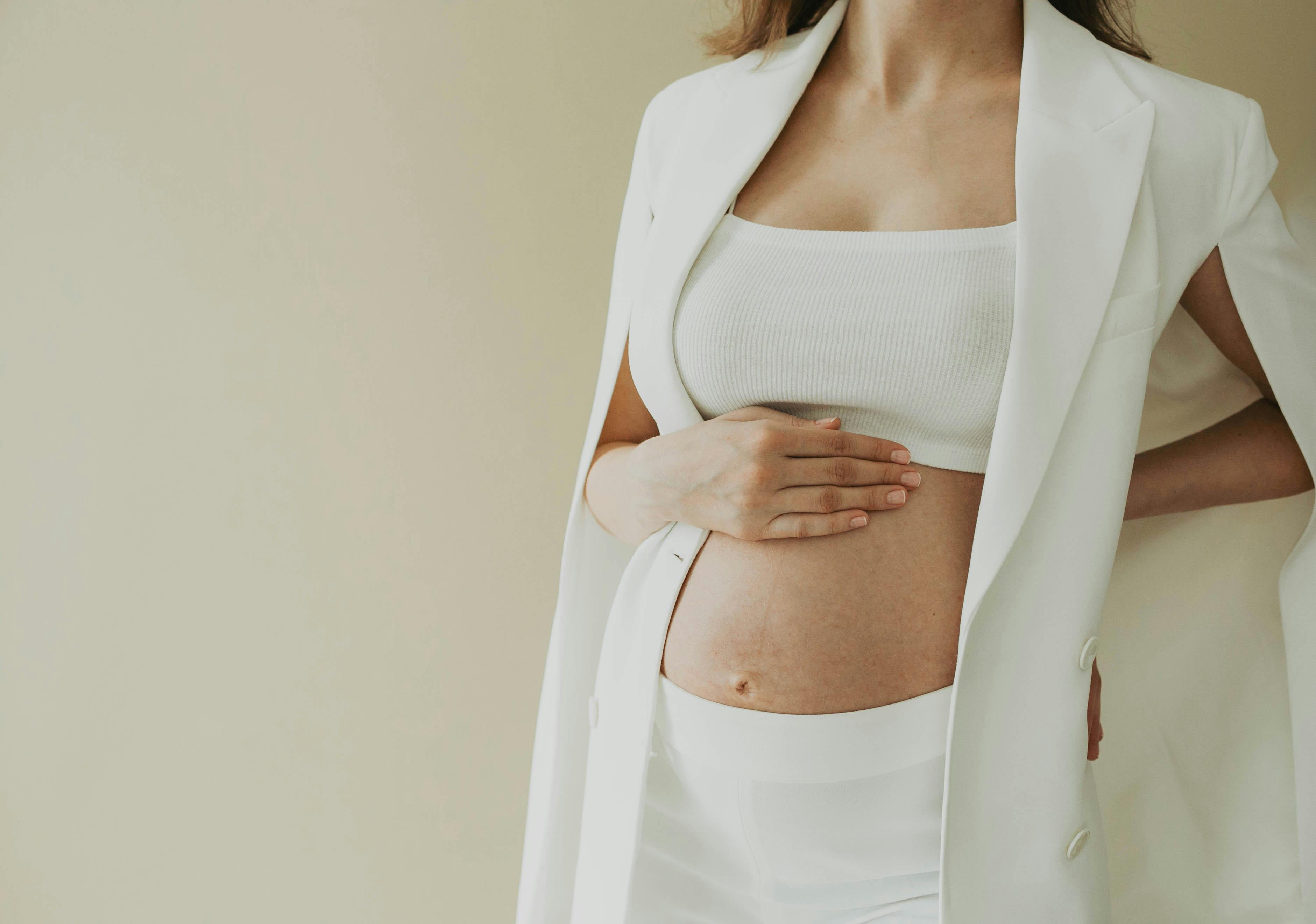 Close-up of a pregnant woman in fashionable attire posing in a studio setting.