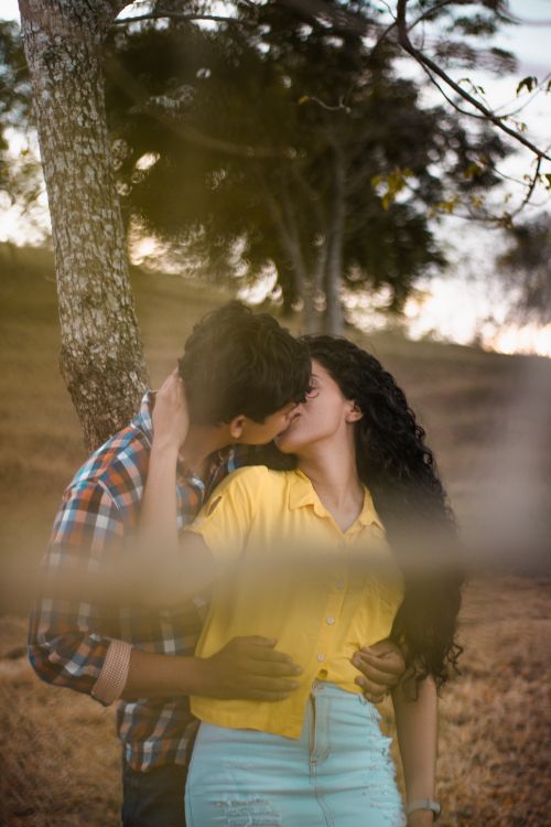 Free A couple kissing under trees during sunset, capturing a romantic moment in nature. Stock Photo