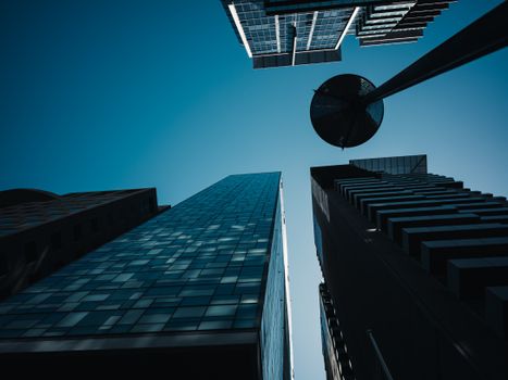 Low angle view of skyscrapers under a clear blue sky with dramatic shadows and a modern urban pole.