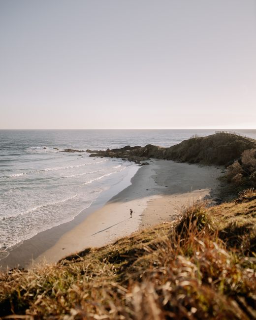 A serene beachscape at sunrise in Byron Bay, NSW, Australia with waves and a lone person.