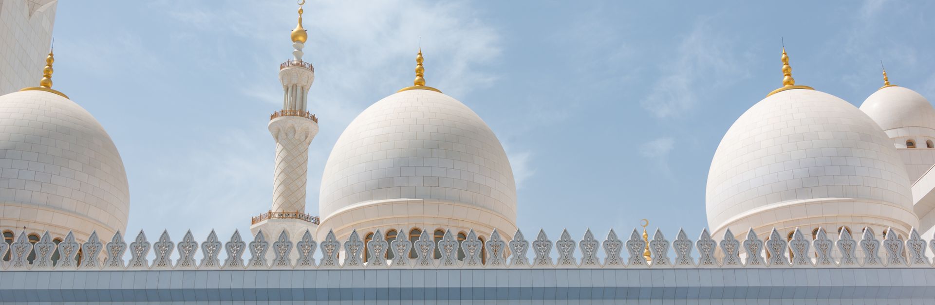 Low angle view of the stunning domes of Sheikh Zayed Grand Mosque under a clear blue sky.