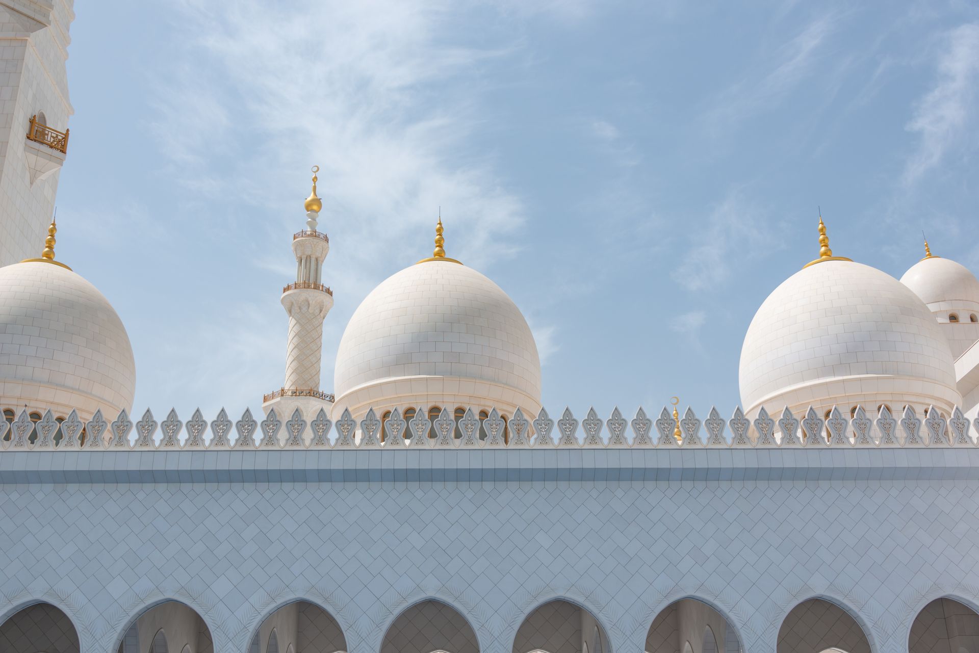 Low angle view of the stunning domes of Sheikh Zayed Grand Mosque under a clear blue sky.