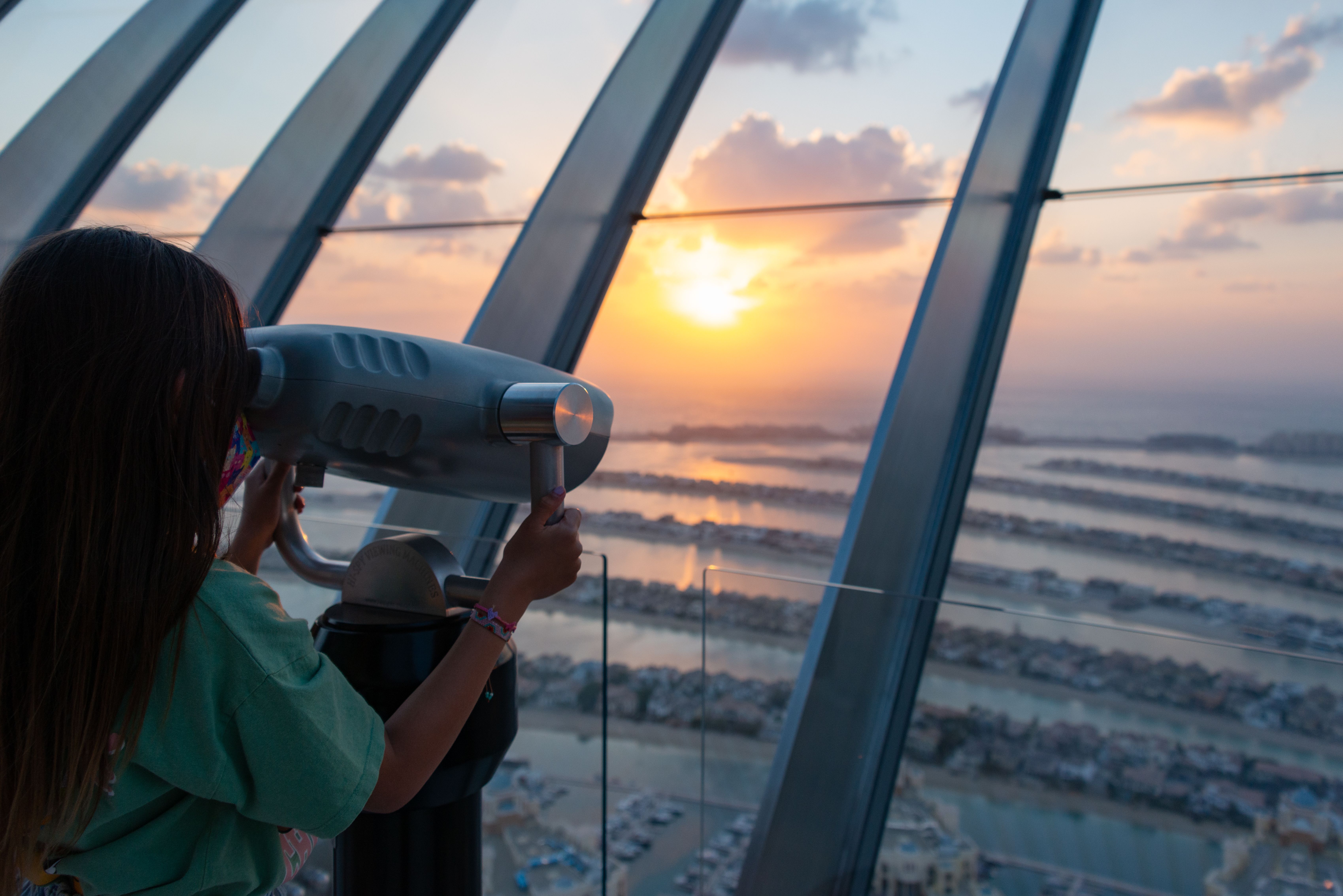 A young girl uses binoculars to view a stunning sunset over Palm Jumeirah in Dubai.
