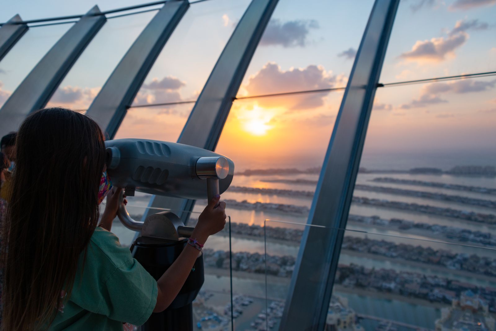 Visitor using a viewing telescope at sunset high above the fronds of Palm Jumeirah