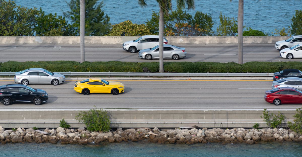 Aerial view of cars on a coastal highway with ocean and palm trees.