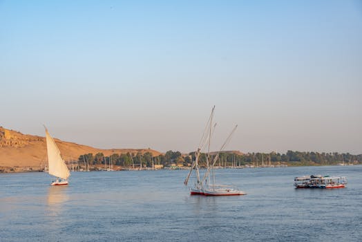 Classic sailboats glide along the Nile with a scenic backdrop of Aswan's desert landscape.
