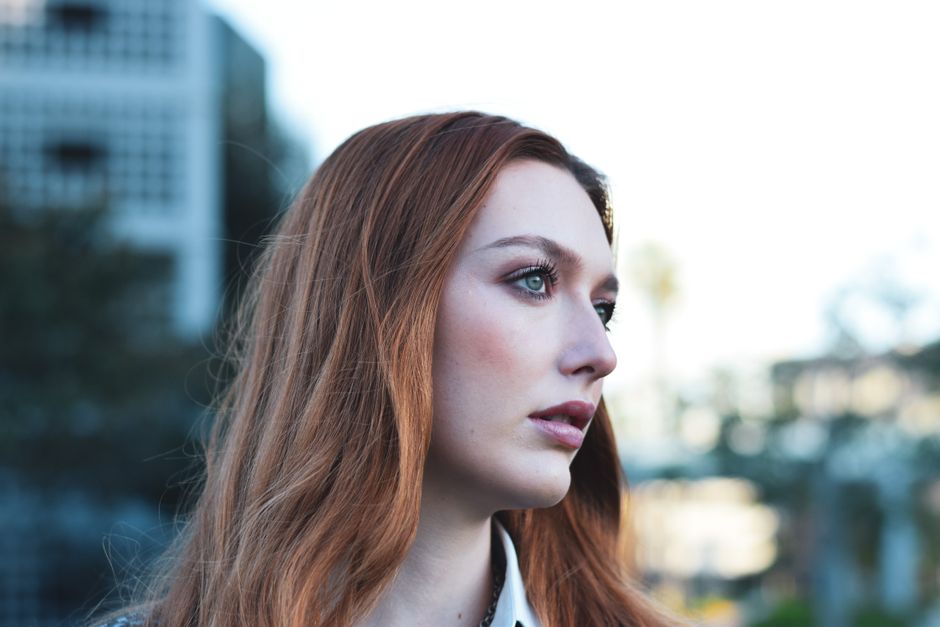 Side profile portrait of a young woman with red hair in an outdoor setting.