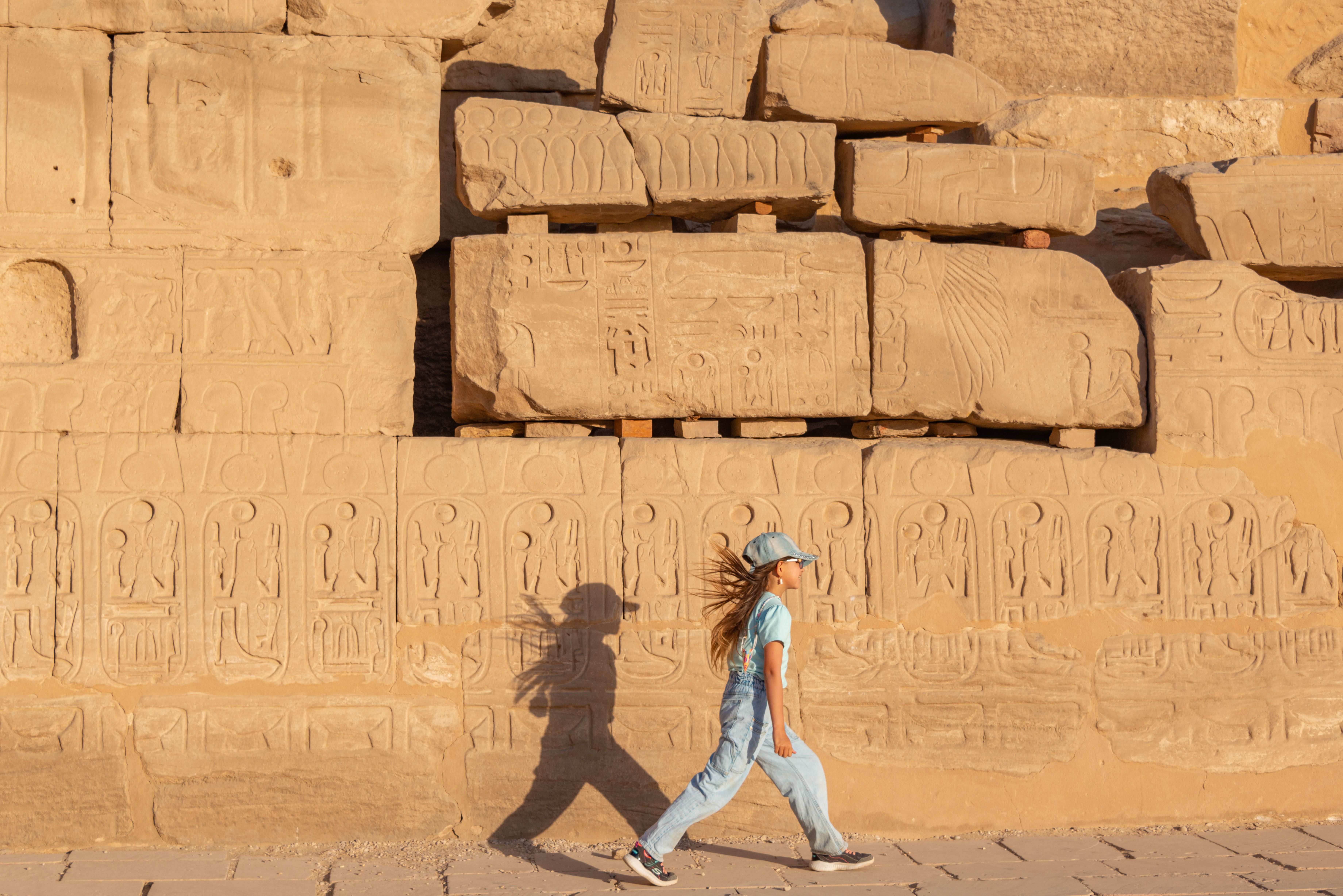 sand art activity for events egypt — A young girl walks past ancient Egyptian hieroglyphs carved into sandstone.