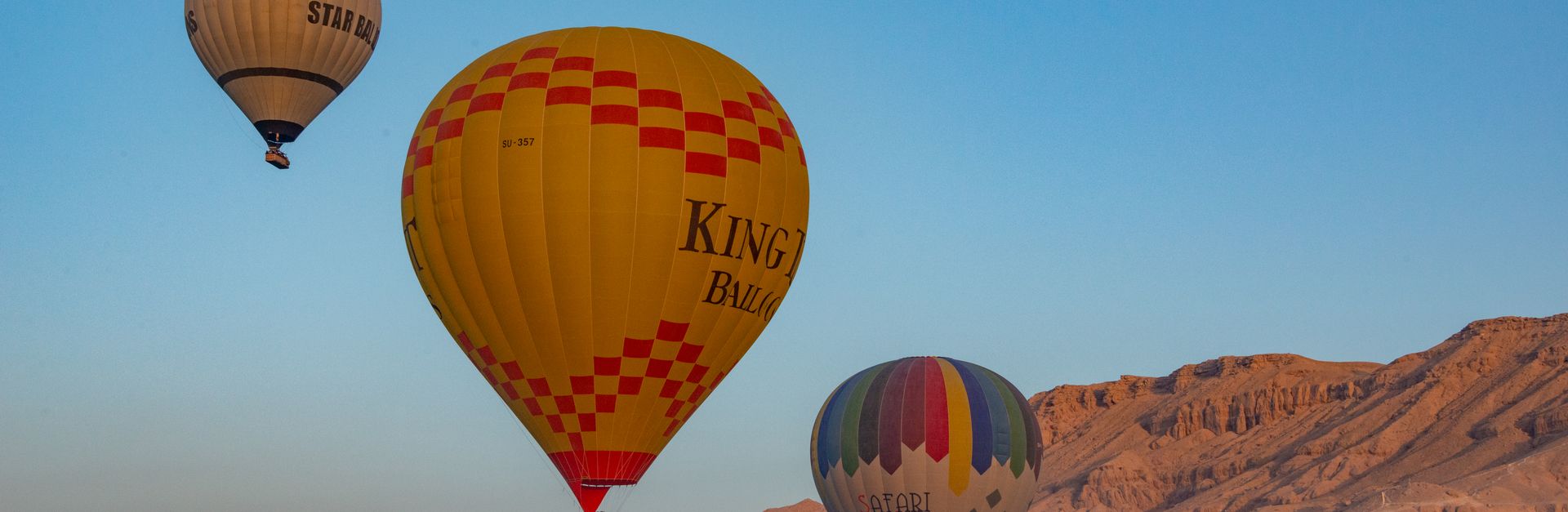 Colorful hot air balloons soar over Luxor's scenic desert landscape at sunrise.