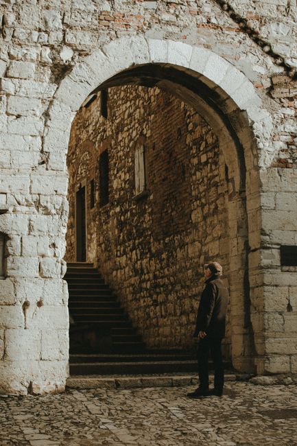 A man stands before an ancient stone archway, admiring its historic architecture.