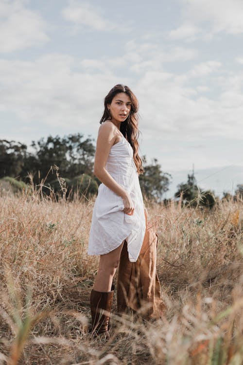 A woman in a white dress and boots standing in a field