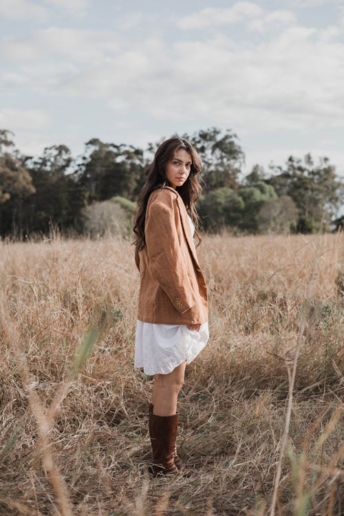 A woman in a brown jacket and boots standing in a field