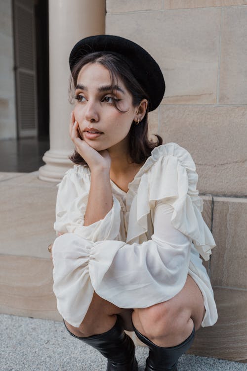 Model in a White Blouse and Black Beret Crouching by the Building