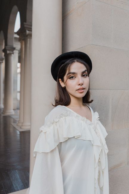 Woman in stylish attire poses gracefully against stone pillars in a historical setting.