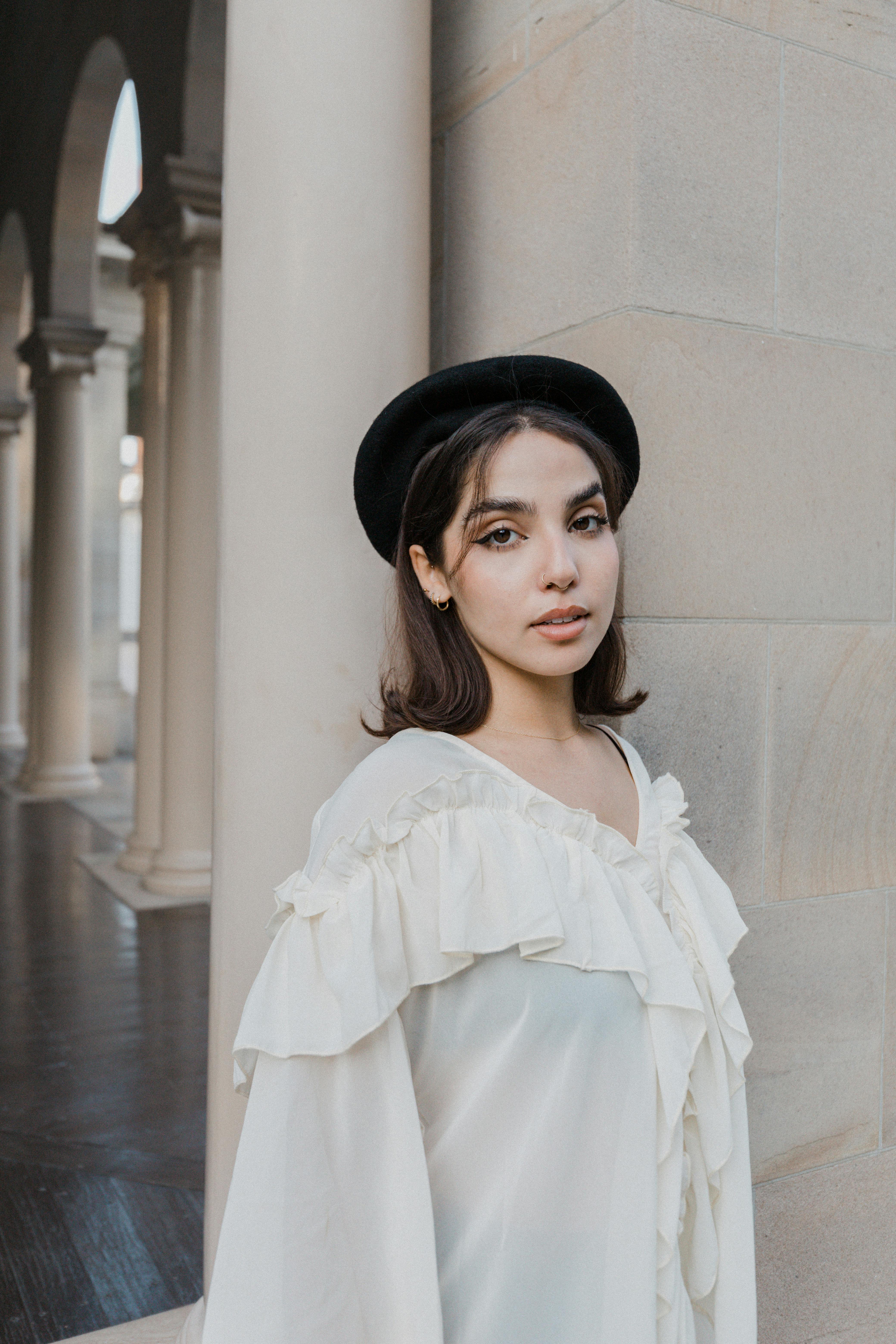 grátis Mulher em traje elegante posa graciosamente em frente a pilares de pedra em um cenário histórico. Foto profissional