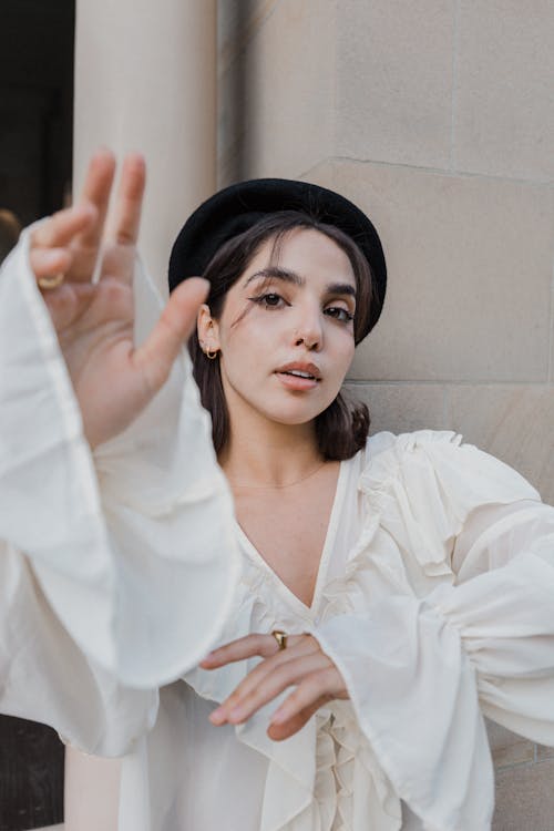 A woman in a white shirt and black hat is making a gesture