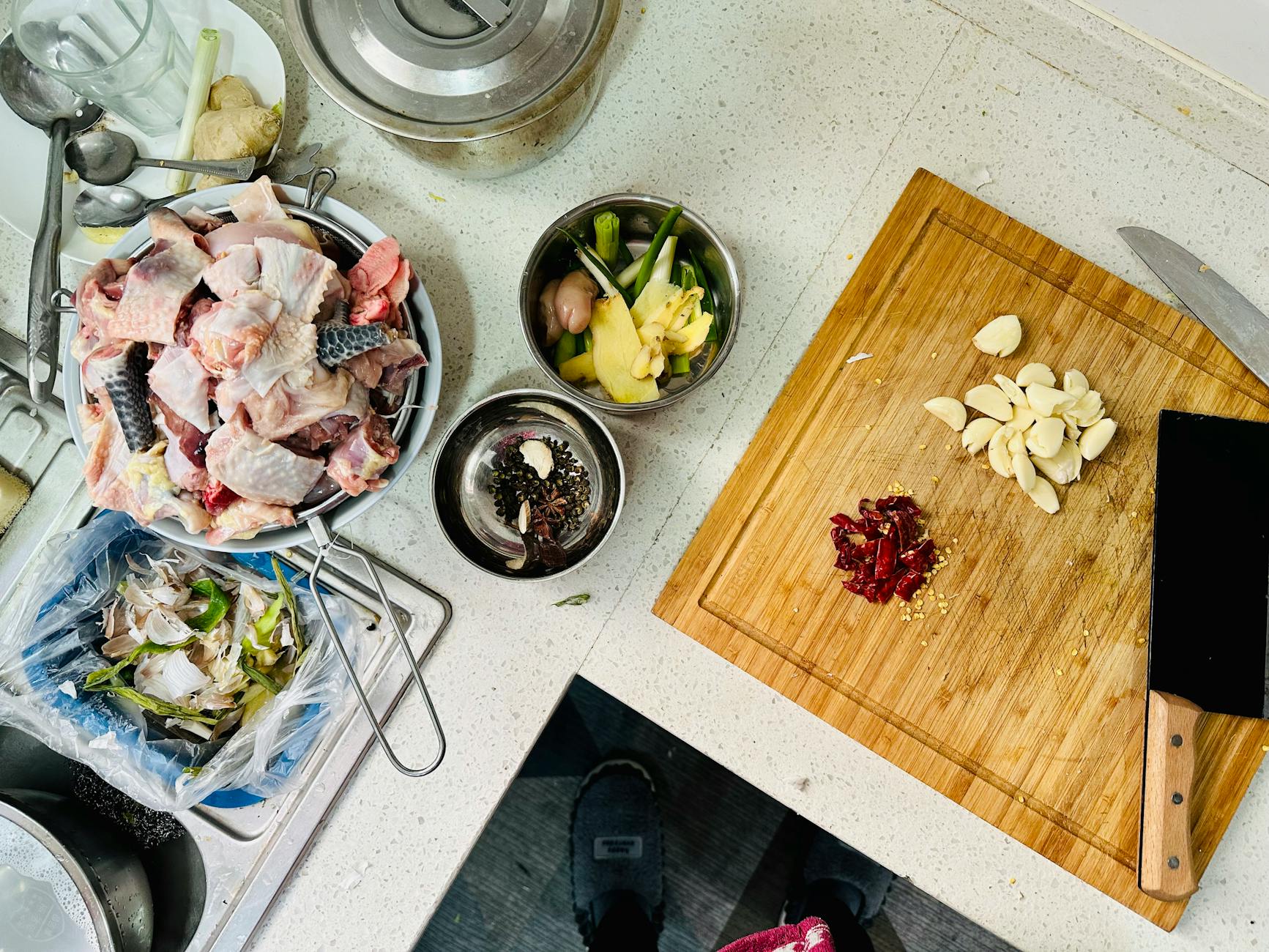 Overhead shot of a kitchen counter with chopped garlic, chicken, and various ingredients for cooking preparation.