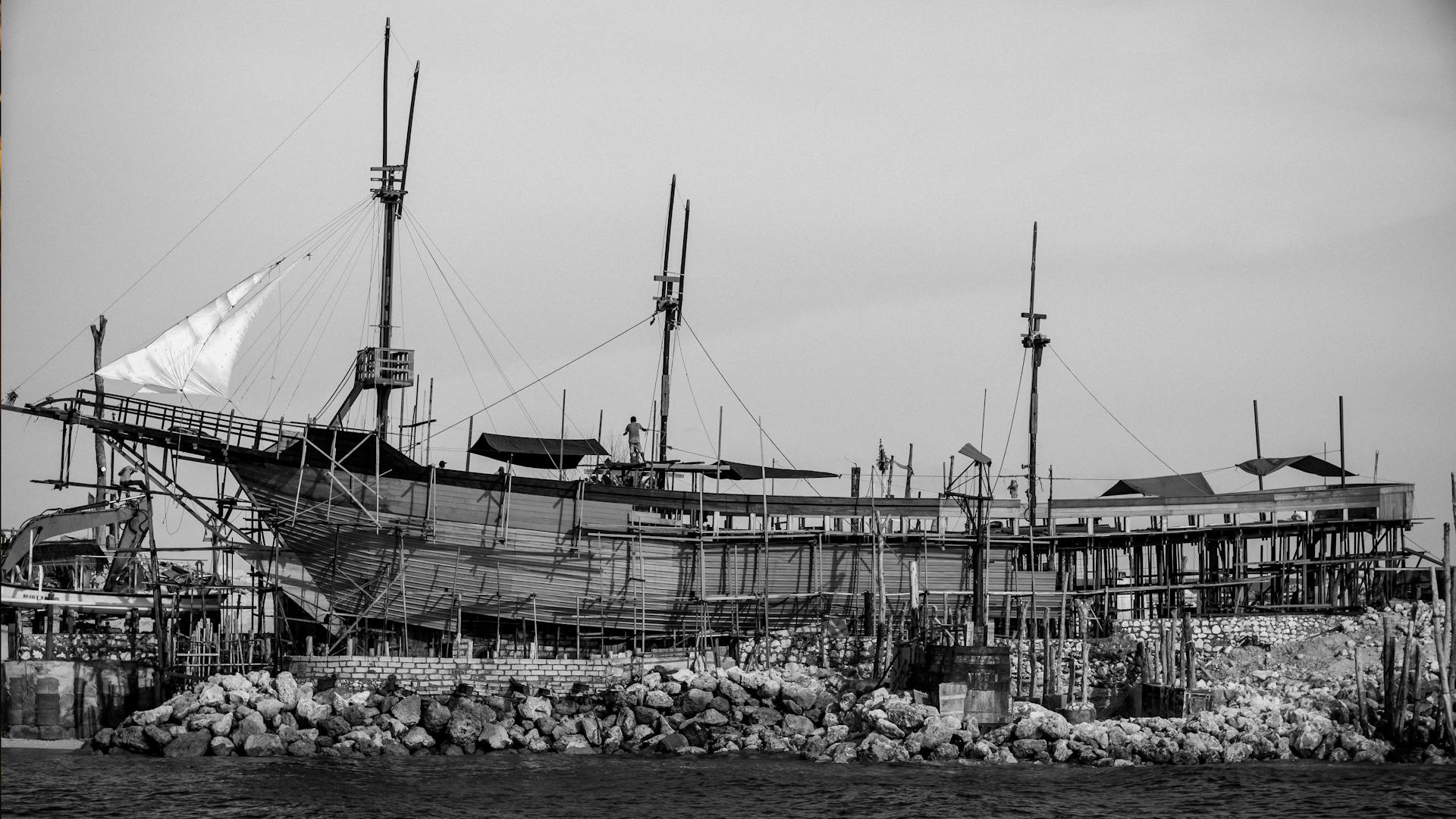 Monochrome photo of a traditional wooden ship under construction at Kuta Beach, Bali.