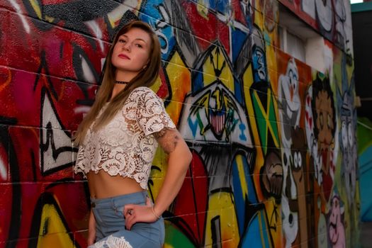 A woman in a white lace crop top poses confidently against a colorful graffiti wall.