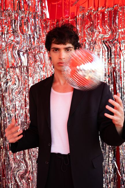 Young man in suit with disco ball against shiny backdrop, exuding modern party vibes.