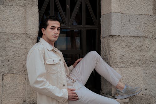 Model in Cream Jacket and White Pants Sitting in the Window