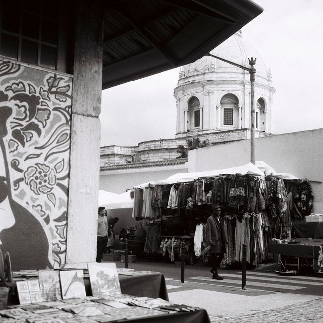 Monochrome view of a lively street market in Lisbon, showcasing clothing stalls and urban architecture.