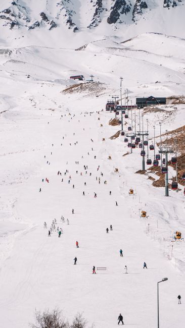 Scenic view of a bustling ski resort with skiers on snowy slopes and cable cars overhead.
