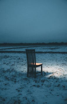 A lone chair illuminated in a snow-covered field during twilight, evoking solitude.